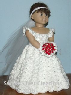 a doll wearing a wedding dress and holding a red flower in her hand on a wooden table