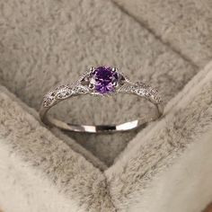 an engagement ring with a purple stone and diamonds on it in a velvet jewelry box