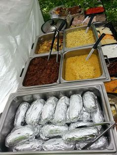 several trays filled with different types of food on display at an outdoor buffet table