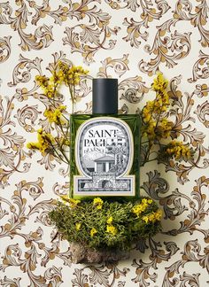 a bottle of cologne sitting on top of a table next to some flowers and plants