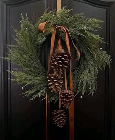 a wreath with pine cones and ribbons hanging on a door