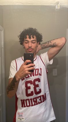 a man taking a selfie in front of a mirror with his cell phone and wearing a basketball jersey