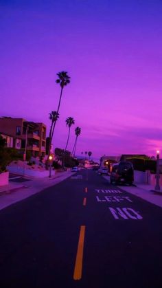 a street with cars parked on the side and palm trees in the background at dusk