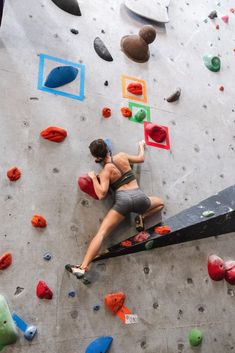 a woman climbing up the side of a wall with colorful rock climbing equipment on it