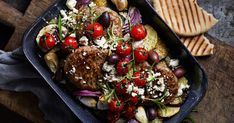 a pan filled with meat and vegetables on top of a wooden table next to crackers