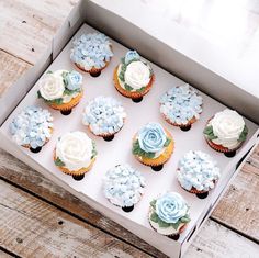 twelve cupcakes with blue and white frosting in a box on a wooden table