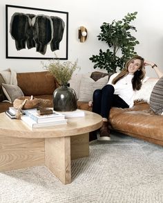 a woman sitting on top of a brown couch next to a table and potted plant