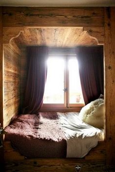 a bed sitting in the corner of a room under a window next to a wooden wall