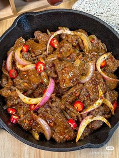 a skillet filled with meat and onions on top of a wooden table