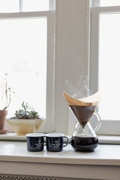 two coffee mugs sitting on top of a table next to a window sill