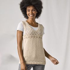 a woman standing in front of a white backdrop wearing grey pants and a beige sweater