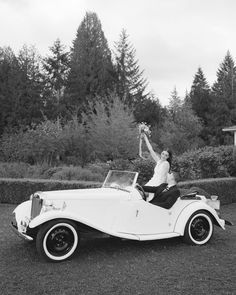 black and white photograph of a woman sitting on top of an old fashioned convertible car