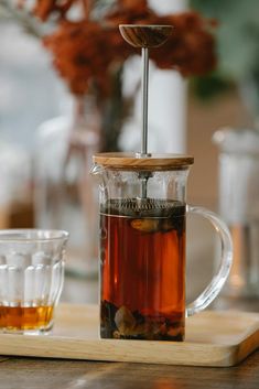 a glass tea pot filled with liquid on top of a wooden tray