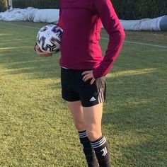 a female soccer player is standing on the field holding a ball and wearing black shorts