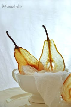 three pieces of fruit in a white bowl on a table with cloths and napkins