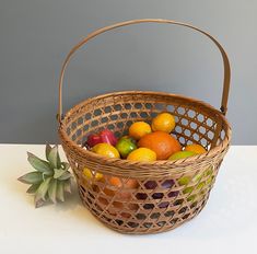 a basket filled with lots of fruit sitting on top of a white table next to a plant