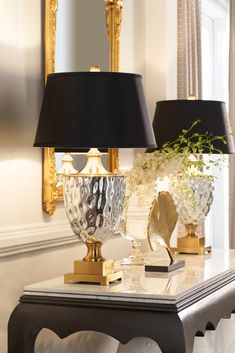 two lamps sitting on top of a white table next to a mirror and gold vase