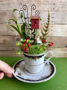 a cup filled with flowers and plants on top of a saucer next to a birdhouse