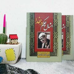 two books with arabic writing on them next to a potted cactus and small house