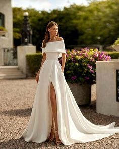 a woman wearing a white wedding dress with a slit in the side, standing outside