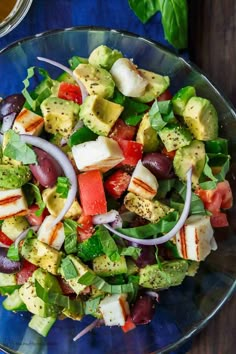 a salad with tomatoes, avocado, onions and other vegetables on a blue plate