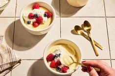 two bowls filled with yogurt and berries on top of a tiled floor next to spoons