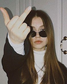 a woman wearing sunglasses making the peace sign with her hand while standing in front of a door