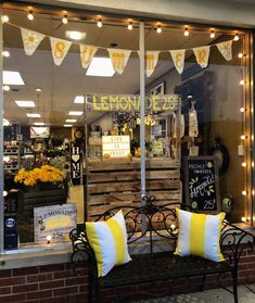 a bench sitting outside of a store front window with yellow and white pillows on it