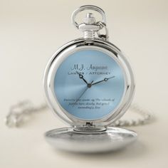 a blue pocket watch sitting on top of a white table next to a silver chain