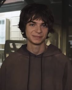 a young man in a brown hoodie smiling at the camera