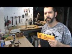 a man holding up a yellow card in his workshop with tools on the table behind him