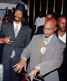 two men in suits and ties are cutting into a piece of cake at a party