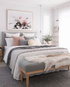 a bedroom with white walls and grey bedding, rugs on the floor, artwork above the bed