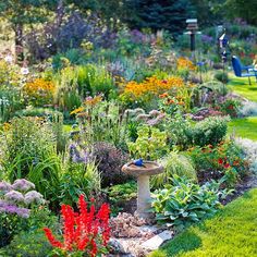 a bird bath in the middle of a garden filled with colorful flowers and greenery