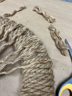 scissors and rope on the ground next to a piece of cloth with two strands of yarn