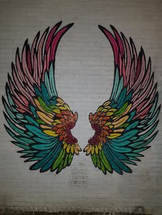 an artistic mural painted on the side of a building with two large colorful wings above it