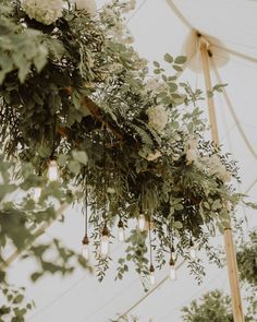 greenery and lights hanging from the ceiling under a tented area for an outdoor wedding