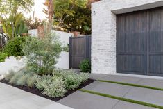 a house with two garage doors and plants in the front garden area on either side of the driveway