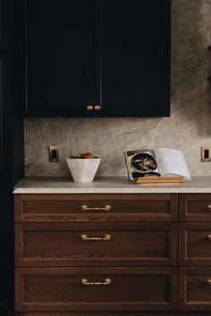 a kitchen with black cabinets and marble counter tops, gold pulls on the handles to match the cabinetry