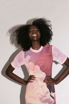 a woman with an afro standing in front of a white wall wearing a colorful dress