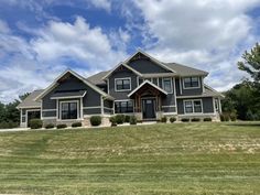 a large gray house sitting on the side of a lush green field under a blue cloudy sky