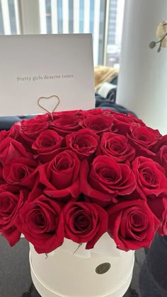 a white box filled with red roses on top of a black table next to a card