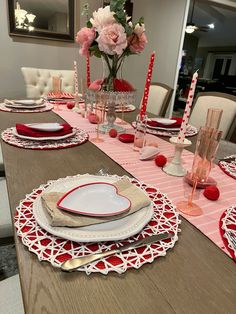 the table is set with red and white plates, silverware, and pink flowers