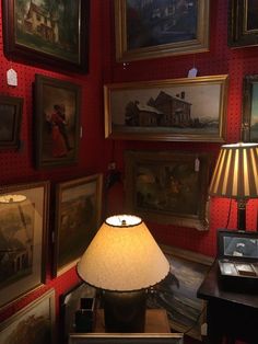 a lamp sitting on top of a wooden table next to pictures and framed paintings in a red room