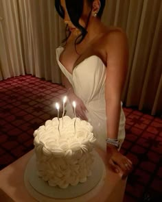 a woman in a white dress standing next to a cake with three candles on it