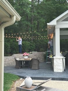 two men are standing on the back porch with string lights strung across the patio area