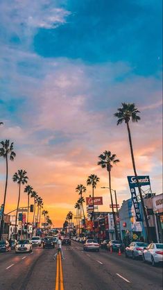 the sun is setting on an empty street with palm trees in the foreground and cars driving down the road