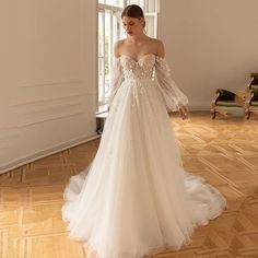 a woman in a white wedding dress standing on a wooden floor next to a window