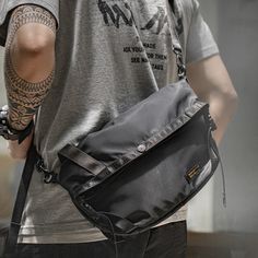 a man carrying a black messenger bag on his left hand and tattoos on his right arm