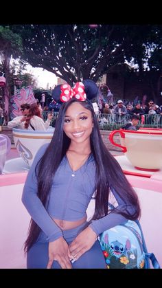 a woman sitting on top of a pink bench in front of a building with minnie mouse ears